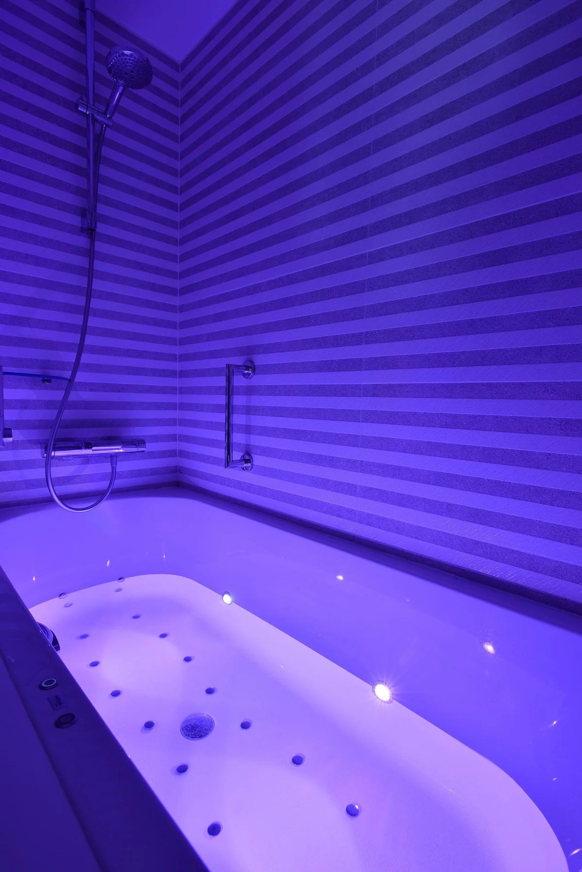 Baignoire avec éclairage violet, carrelage à rayures en arrière-plan.